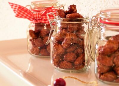 Auf einem Regal stehen drei Einweckgläschen mit gebrannten Mandeln und weihnachtlichen Schleifen.